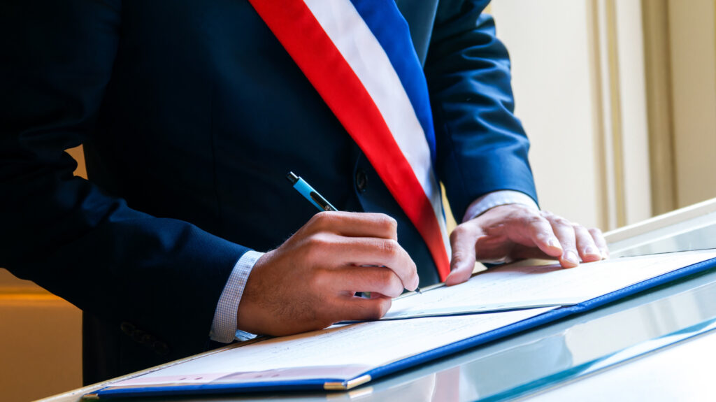 Un maire, avec l'écharpe, signe un document officiel